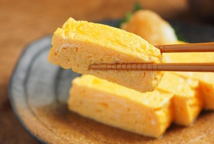 Tamagoyaki abilmente mangiato con le bacchette (hashi).